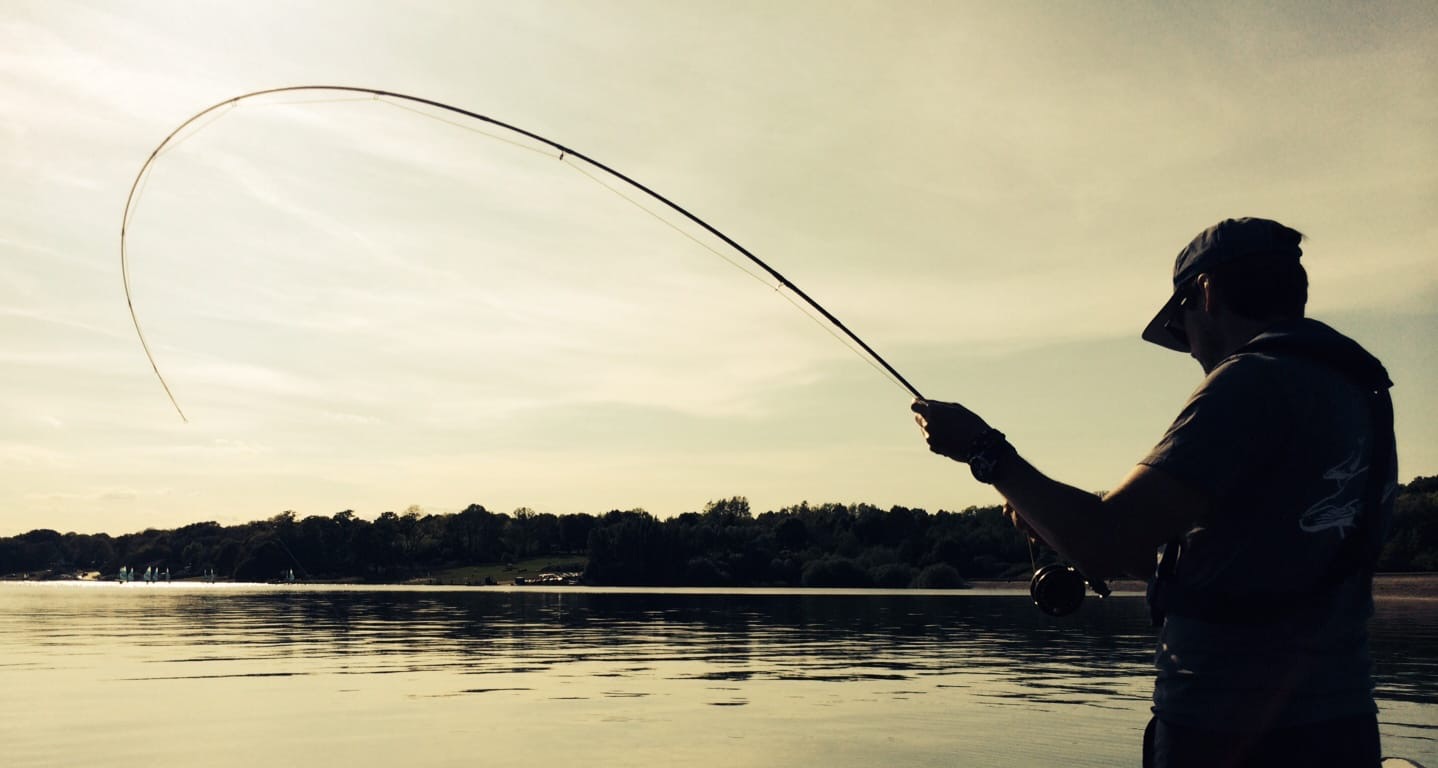 Single angler casting with a bent rod on a wide lake view